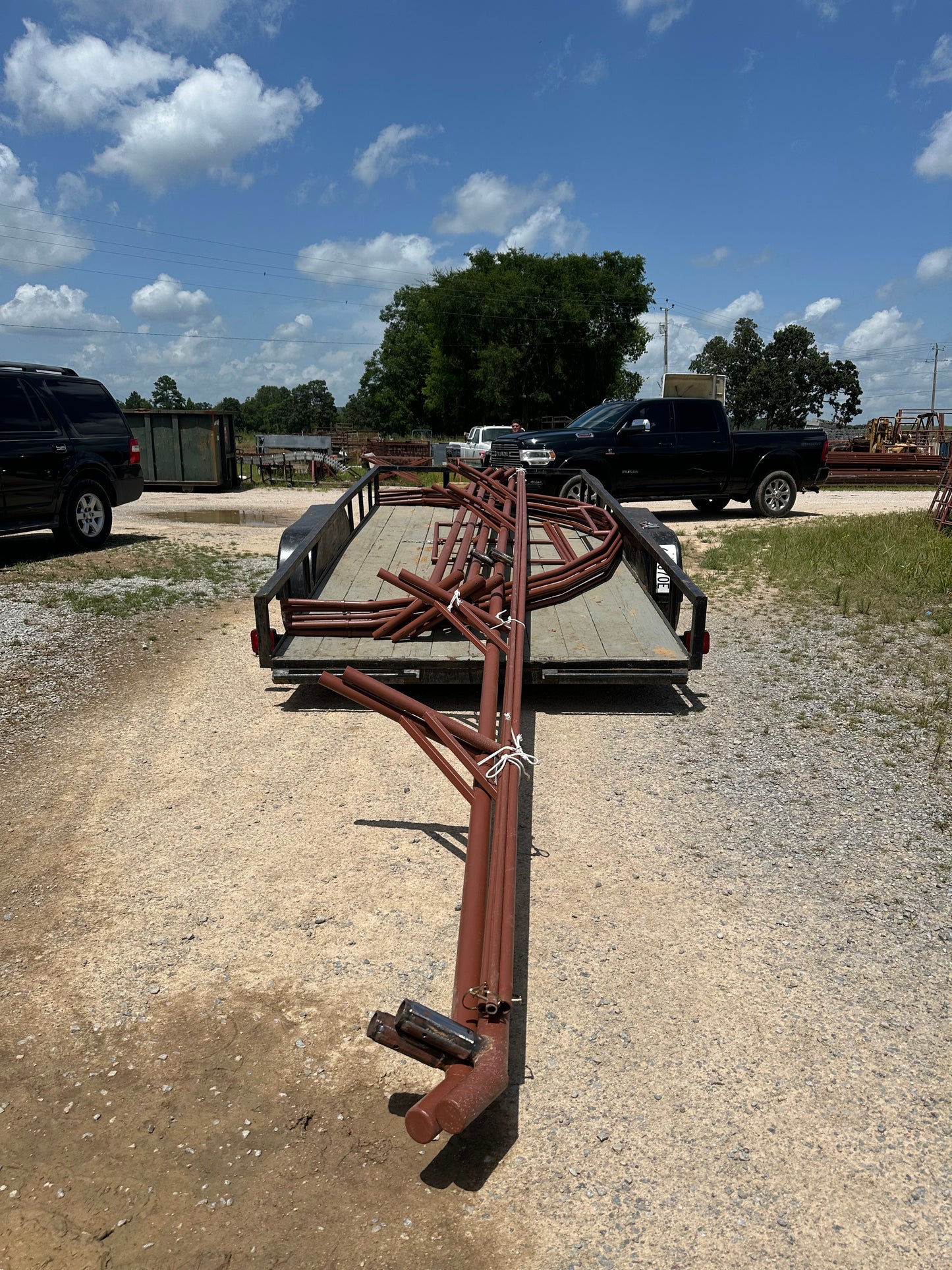 Large steel frame loaded on a flat trailer on a gravel surface with a blue sky and trees in the background