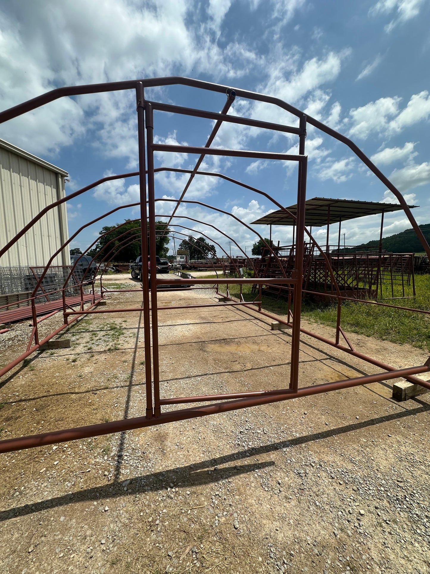Metal archway structure on a gravel driveway with a blue sky and clouds in the background.