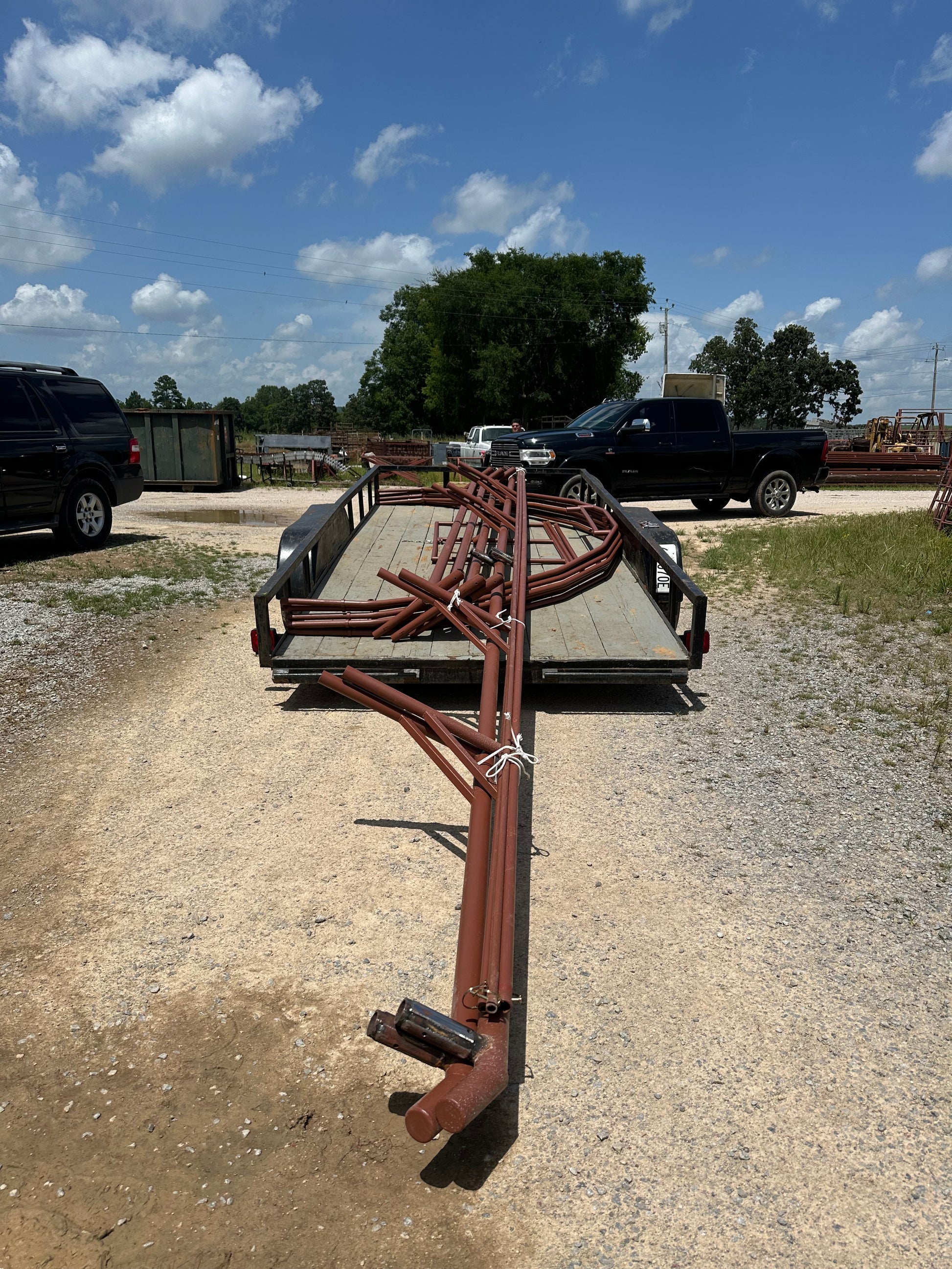 Large steel frame loaded on a flat trailer on a gravel surface with a blue sky and trees in the background